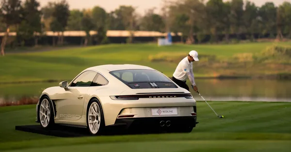 A white Porsche 911 on a golf course with a golfer behind it