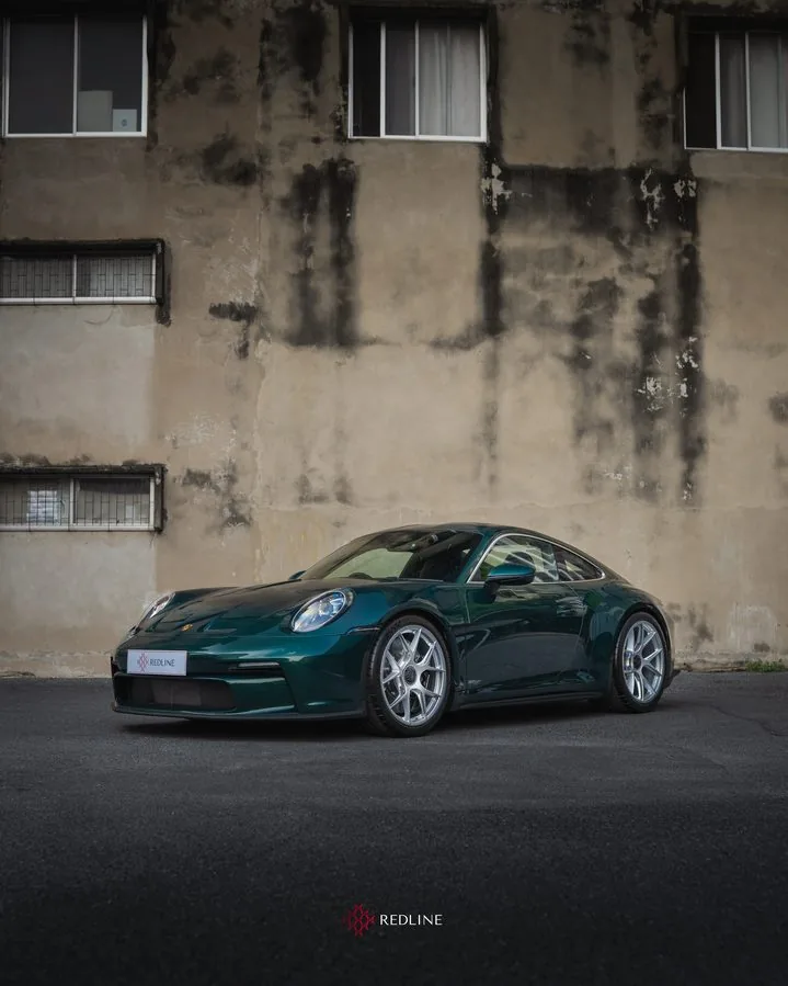 A green Porsche 911 in front of a concrete wall